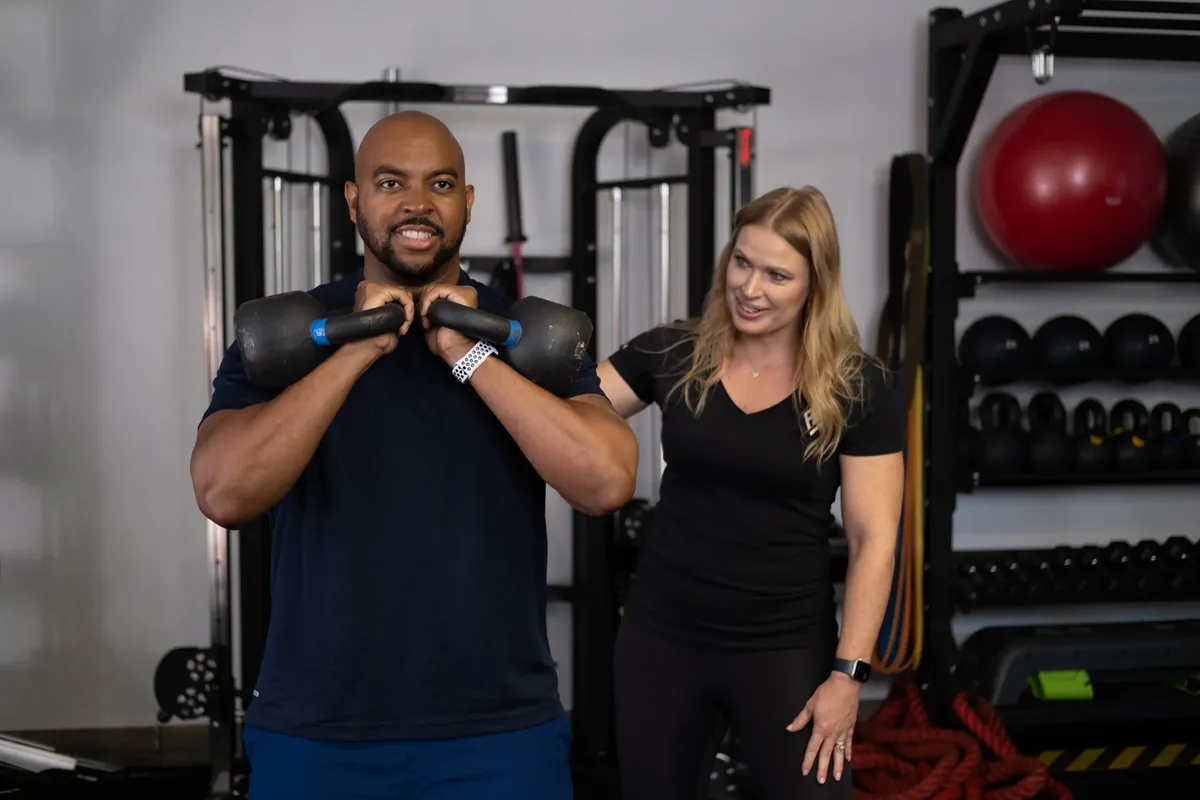 A coach watching a client hold two kettlebells at Formula Fitness