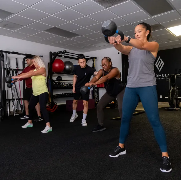 Clients and a coach doing kettlebell swings in the Formula Fitness studio