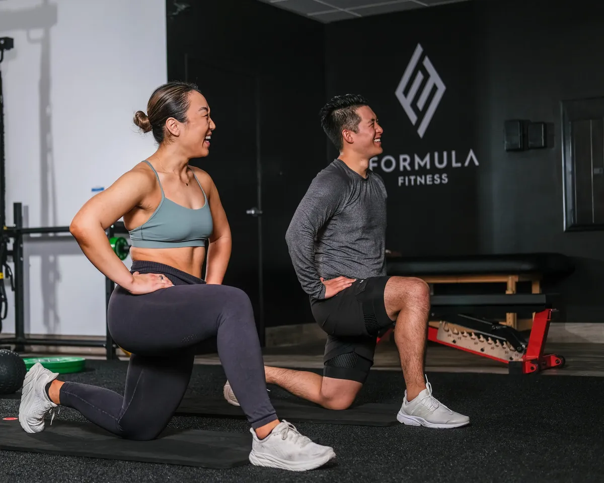 Two people laughing during a half-kneeling lunge in the Formula Fitness studio